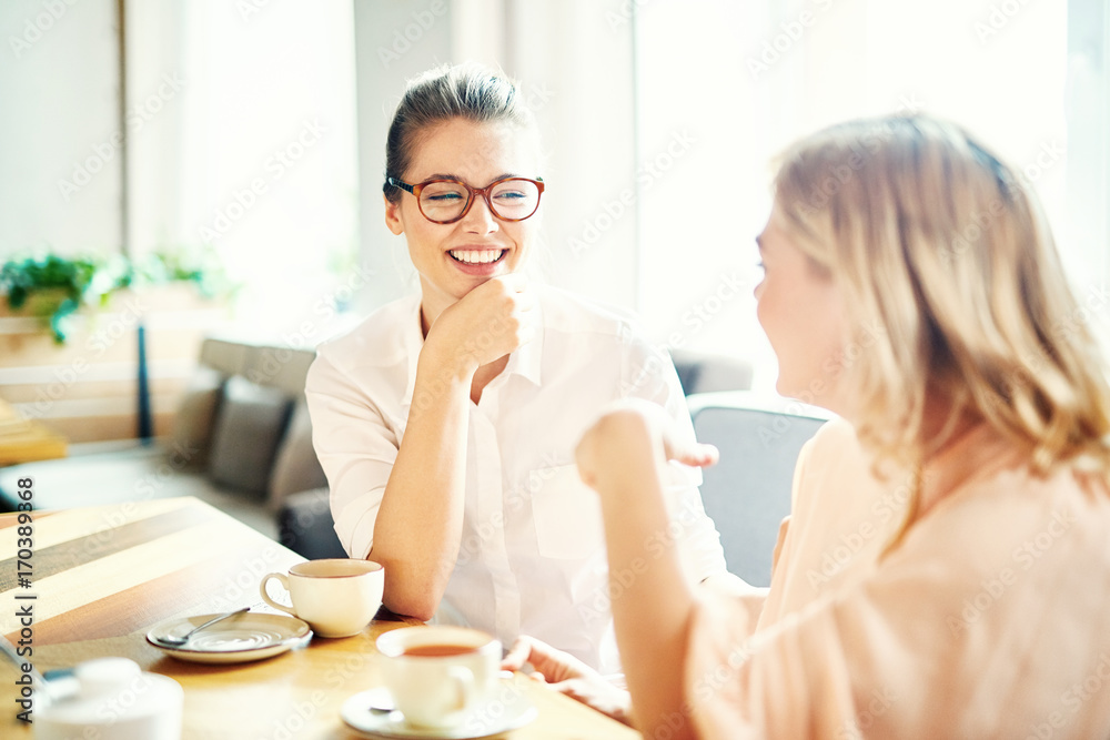 Lovely moments of friendship: cheerful young women gathered together at cozy small cafe and chatting animatedly with each other Lovely moments of friendship: cheerful young women gathered together at cozy small cafe and chatting animatedly with each other