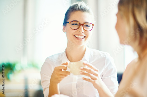 Head and shoulders portrait of attractive young woman with charming smile enjoying fragrant coffee while hanging out with best friend in cozy small cafe © pressmaster