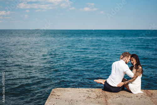 Young couple are sitting on the pier by the sea