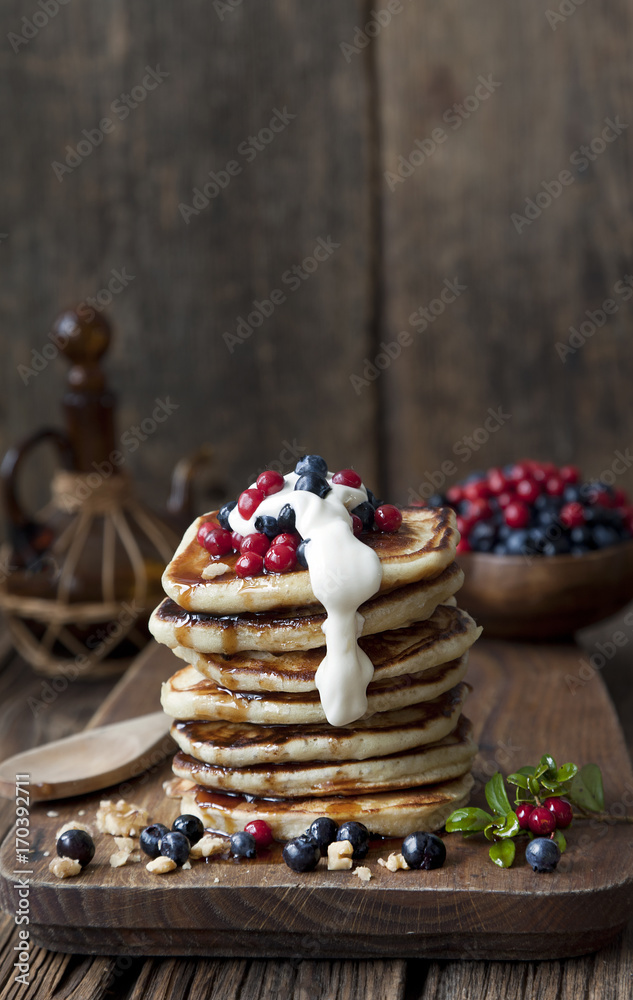 Delicious homemade pancakes, fritters with sour cream and fresh forest berries on rustic wooden background. Selective focus, background