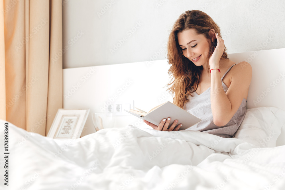 Young happy pretty lady sitting on bed indoors Young happy pretty lady sitting on bed indoors