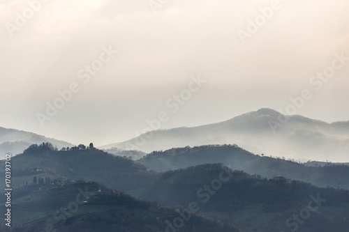Green hills and trees in the foreground, mist and other hills and mountains in the background