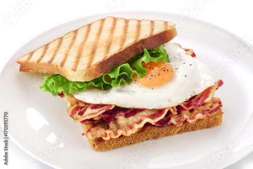 Sandwich with bacon, fried egg and lettuce on a plate.