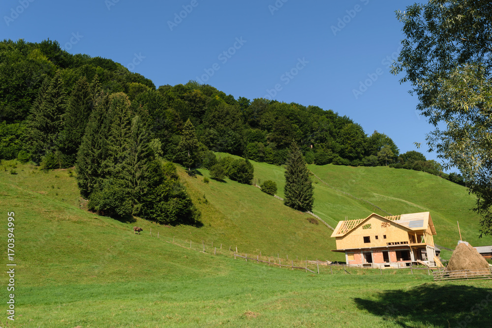 house under construction in the green hills covered with green forest and clear blue sky