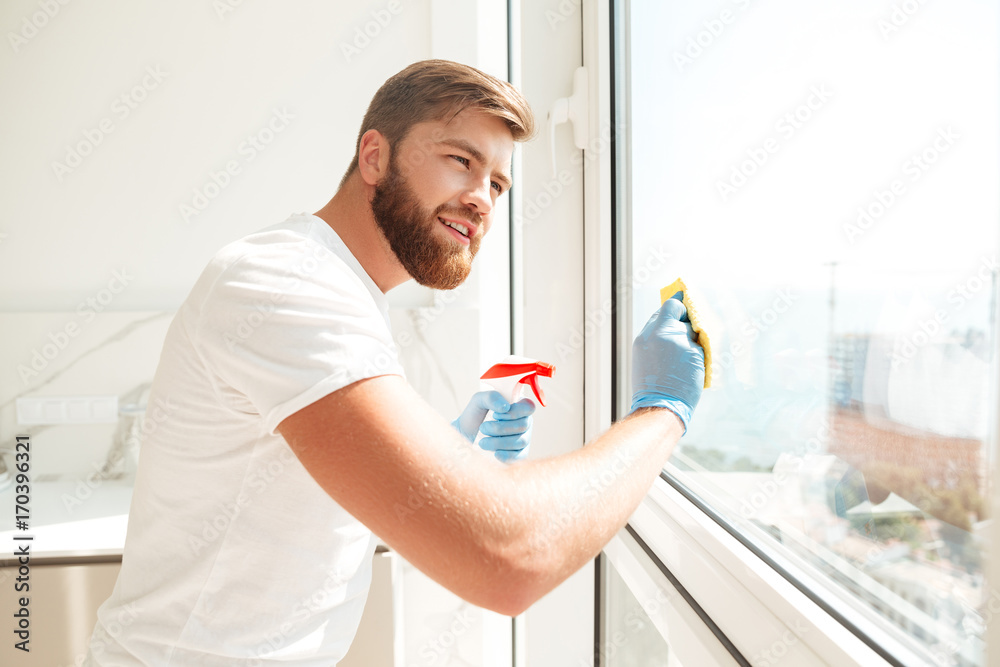 Fototapeta premium Side view of smiling bearded man wipes a window
