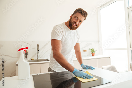 Smiling casual bearded man wipes a stove on kitchen
