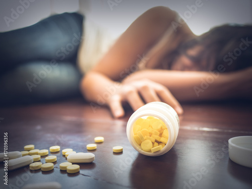 Woman taking medicine overdose and lying on the wooden floor with open pills bottle. Concept of overdose and suicide. photo