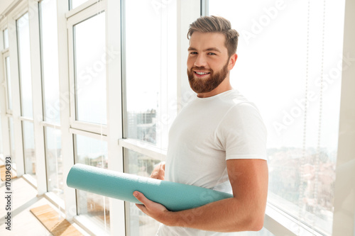 Side view of Smiling bearded man standing with fitness mat