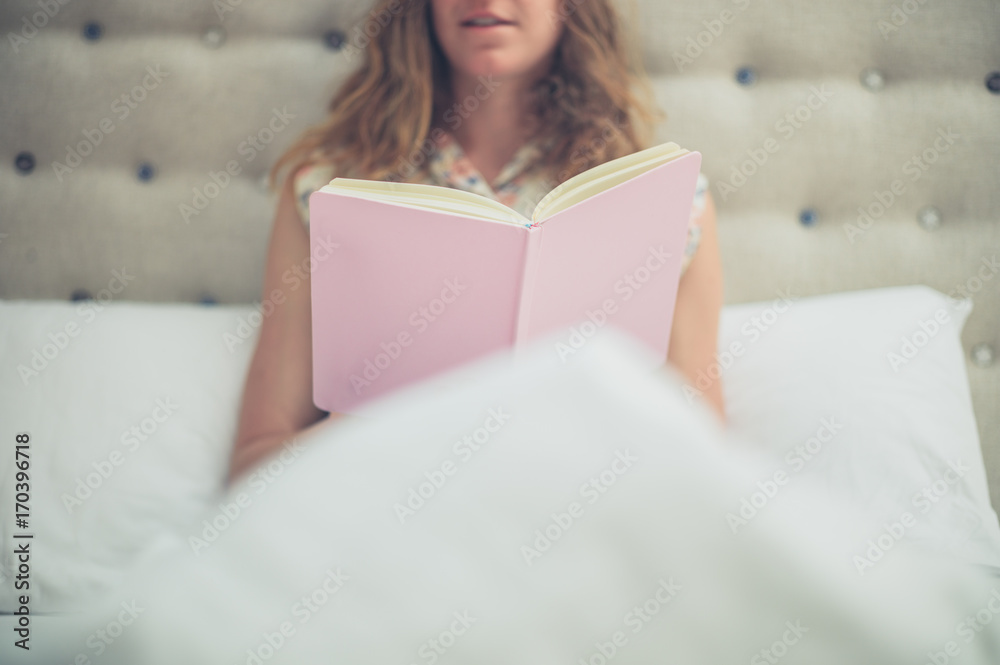 Woman reading pink book in bed Woman reading pink book in bed