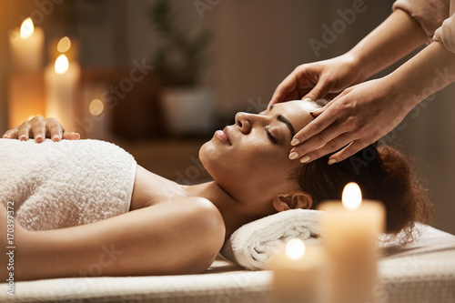 Attractive african girl enjoying face massage in spa salon. photo