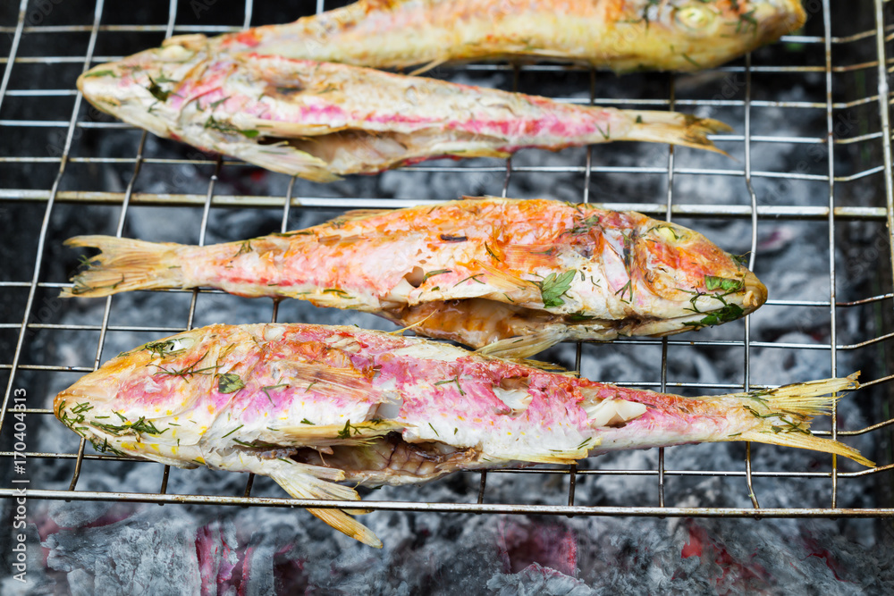 Grilled fish with spices on fire. Grilling fish surmullet on campfire (BBQ). Closeup, selective focus