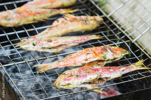 Grilled fish with spices on fire. Grilling fish surmullet on campfire (BBQ). Closeup, selective focus
