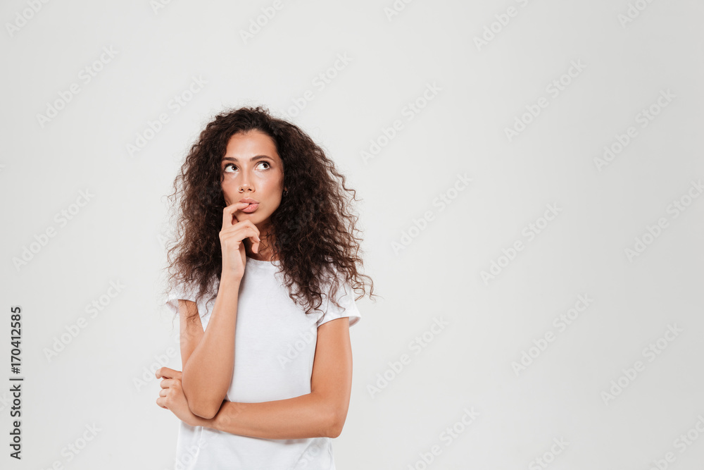 Pensive curly woman with finger near the mouth looking away Pensive curly woman with finger near the mouth looking away