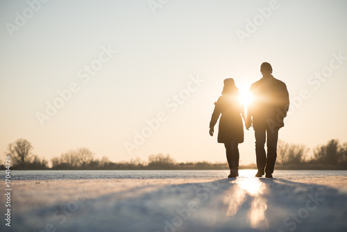 Couple walking through frozen lake as sun sets