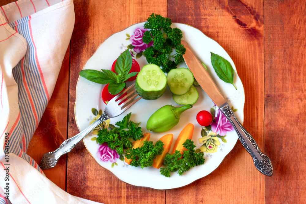 Fresh raw greens, vegetables on wooden background, white ceramic plate in center, top view, copy space. Healthy, clean eating, vegan, detox, dieting food concept