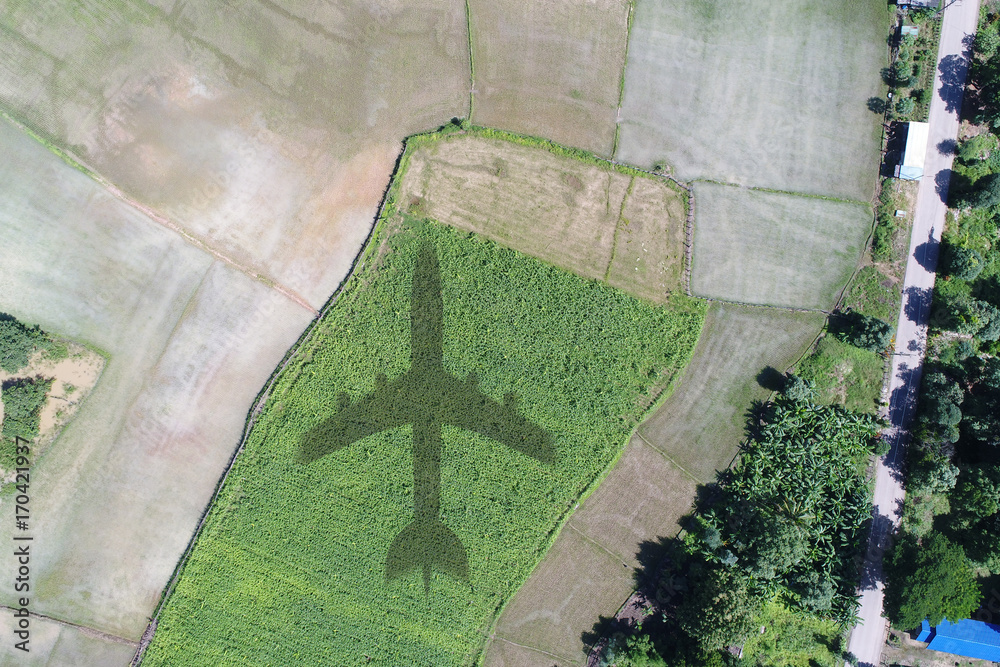 Fototapeta premium Airplane shadow or Airplane silhouette on landscape village countryside and green filed trees nature and mountain background - Aerial view take a photo by drone camera