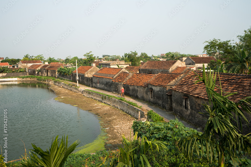 Vietnam landscape with old aged houses and woman cycling on road in village