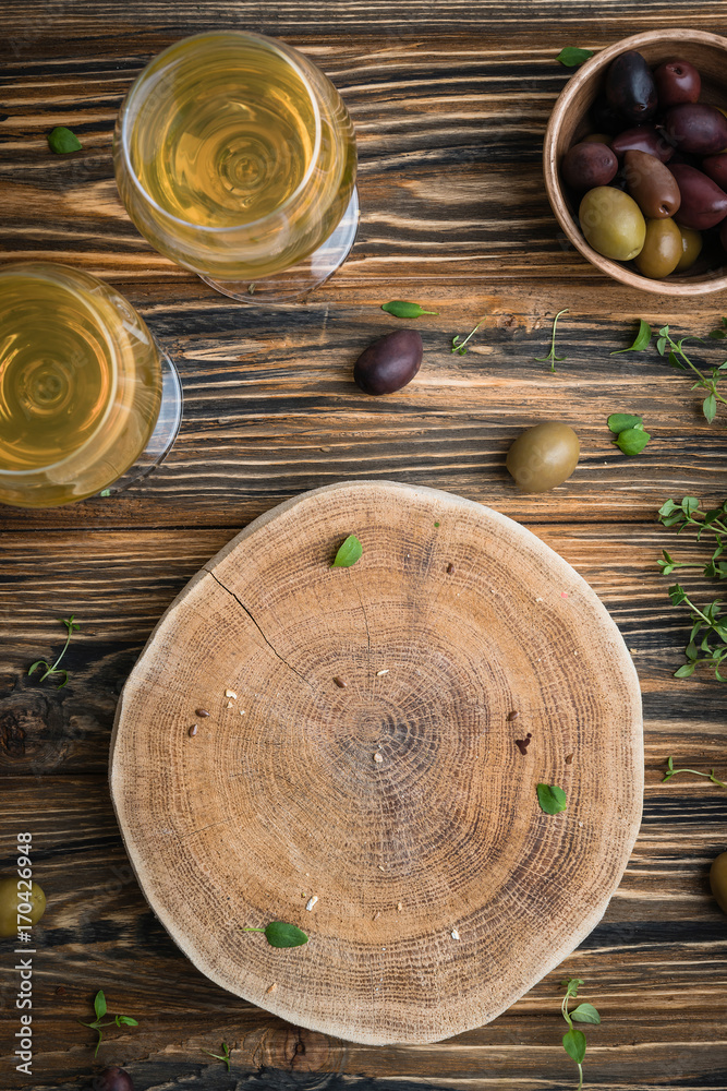 Empty wooden board with blank space for text with olives and fresh thyme, served with two glasses of white wine. Healthy meal concept on wooden rustic table. Top view