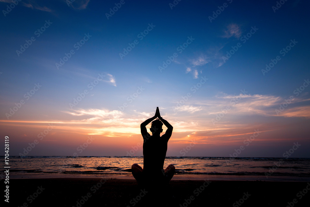 Young healthy man practicing yoga on the beach at sunset