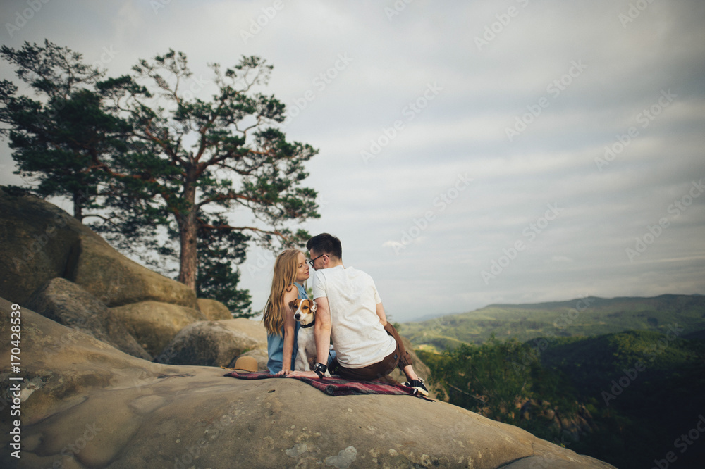 Young couple in love resting on peak of mountain in summer. Couple spreading a blanket for picnic
