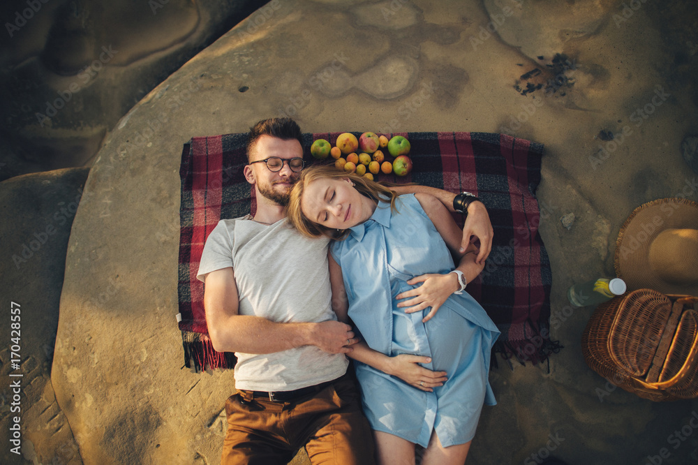 couple in love on a white plaid in a field on a picnic. against a background of a sunset in the mountains. romance couple in love on a white plaid in a field on a picnic. against a background of a sunset in the mountains. romance