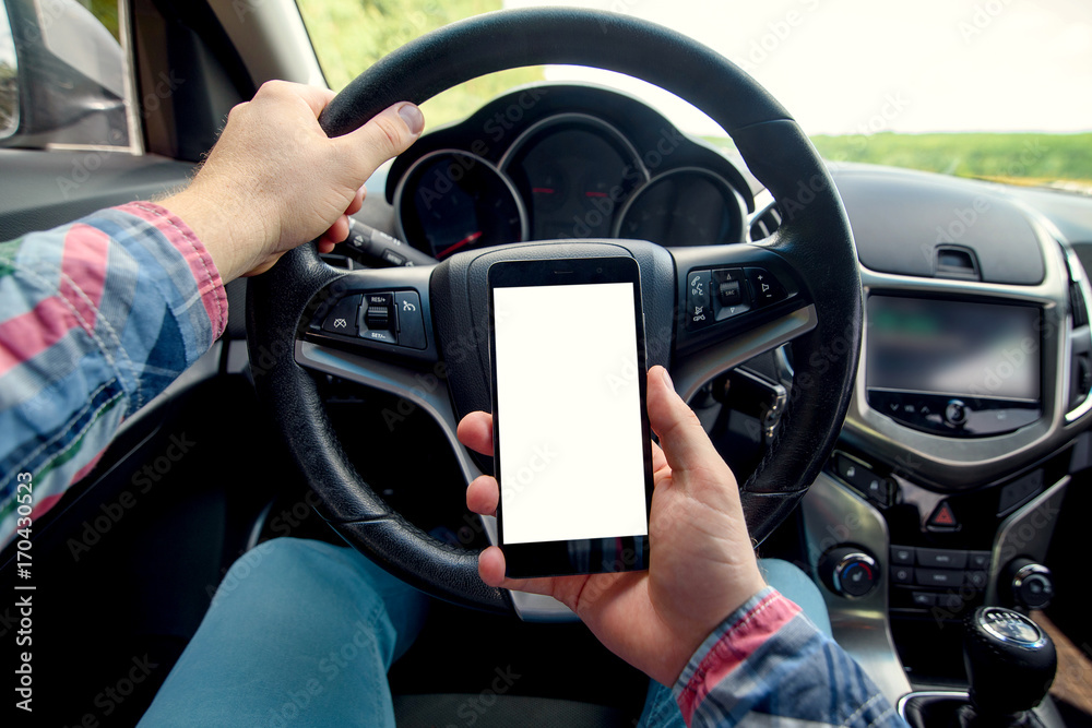 Close-up of man driver using smart phone in car. Driver sitting in car and holding mobile smart phone with isolated screen. Modern smartphone with white blank screen, copy space for text or design Close-up of man driver using smart phone in car. Driver sitting in car and holding mobile smart phone with isolated screen. Modern smartphone with white blank screen, copy space for text or design
