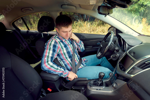 Handsome serious young man in plaid shirt fastening seat belt in car. Businessman putting on his seat belt in his car. Transportation and vehicle concept © mirage_studio