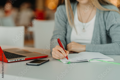 hands of female writing on notebook in cafe with laptop, smart phone and cup of coffee