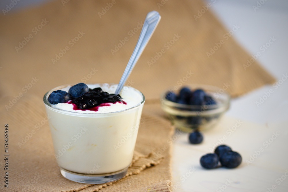 Glass cup of yogurt with blueberries on white table and white background Glass cup of yogurt with blueberries on white table and white background