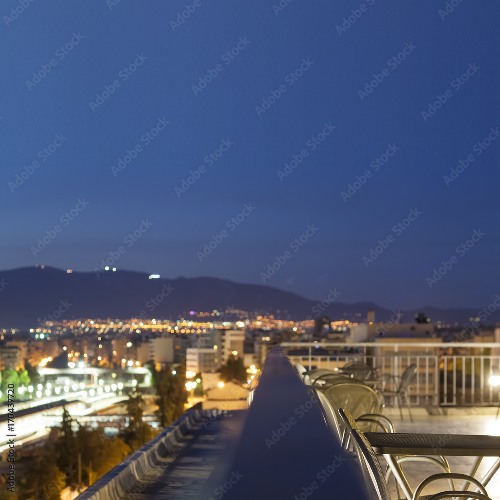 Panoramic terrace in Athens, Greece. Skyline night view, railing, chairs and tables.  Blurred photo, selective focus, copyspace, perfect as background.