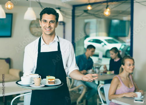 Waiter holding served tray meeting visitors at pastry bar