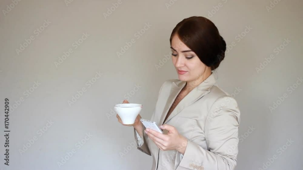 Beautiful young businesswoman dials a number on the mobile phone, calls and talks on cellphone and drinks coffee Beautiful young businesswoman dials a number on the mobile phone, calls and talks on cellphone and drinks coffee