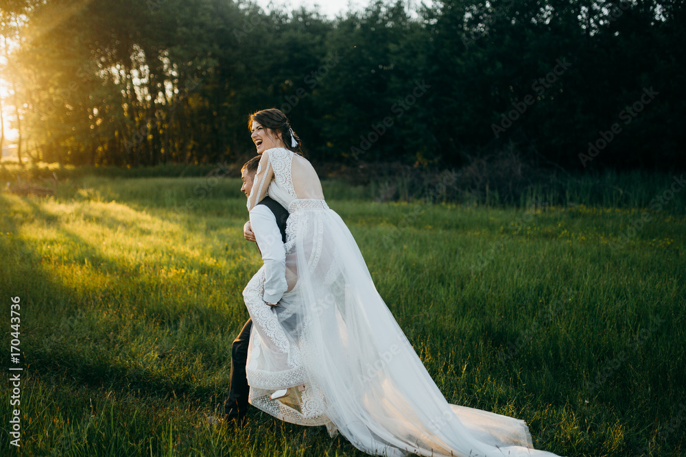Wonderful groom and bride are walking around the field at sunset Wonderful groom and bride are walking around the field at sunset