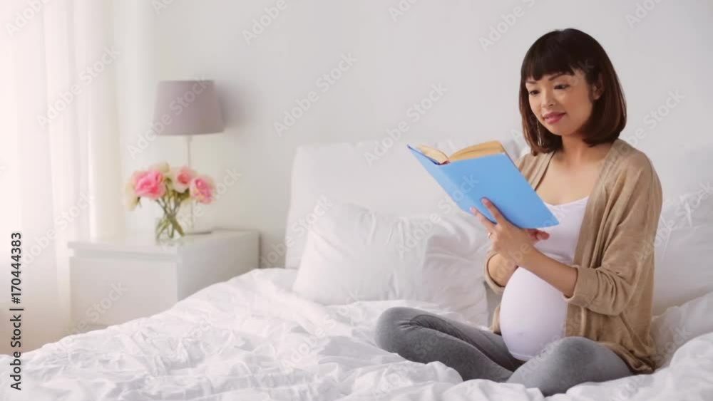 happy pregnant asian woman reading book in bed happy pregnant asian woman reading book in bed