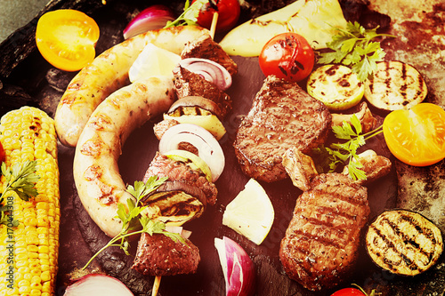 Assorted delicious grilled barbecue meat with vegetable. Beef grilled steaks with spicy sausages, beef kebabs, corn, cherry tomato, pepper, slices of onion, zucchini, eggplant.