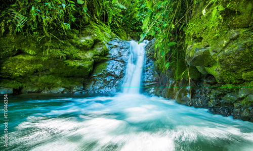 Beautiful small waterfall located inside of a green forest with stones in river at Mindo
