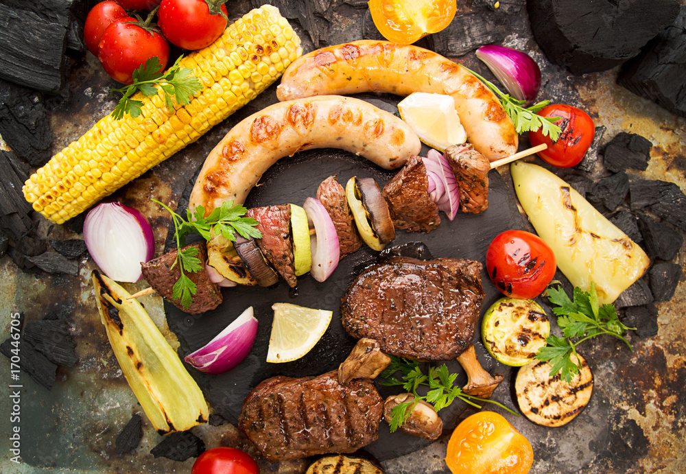 Assorted delicious grilled barbecue meat with vegetable. Beef grilled steaks with spicy sausages, beef kebabs, corn, cherry tomato,  pepper, slices of onion, zucchini, eggplant.