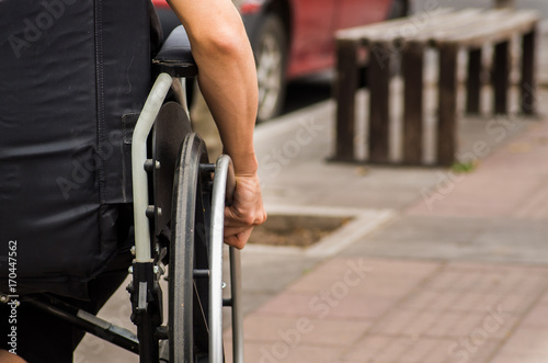 Close-up of male hand on wheel of wheelchair during walk in park