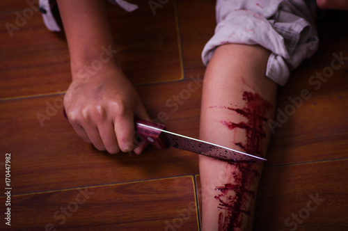 Close up of a young depressive woman holding a knife, with her arm bleeding, in a wooden background photo