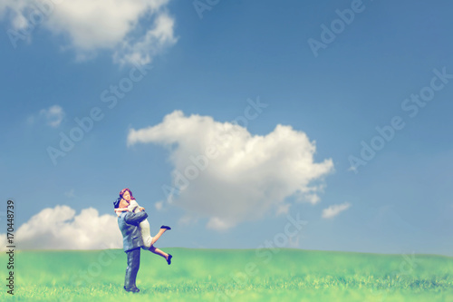 selective focus of miniature couple hugging on grassland and cloudy sky ,abstract background for happy couple concept.