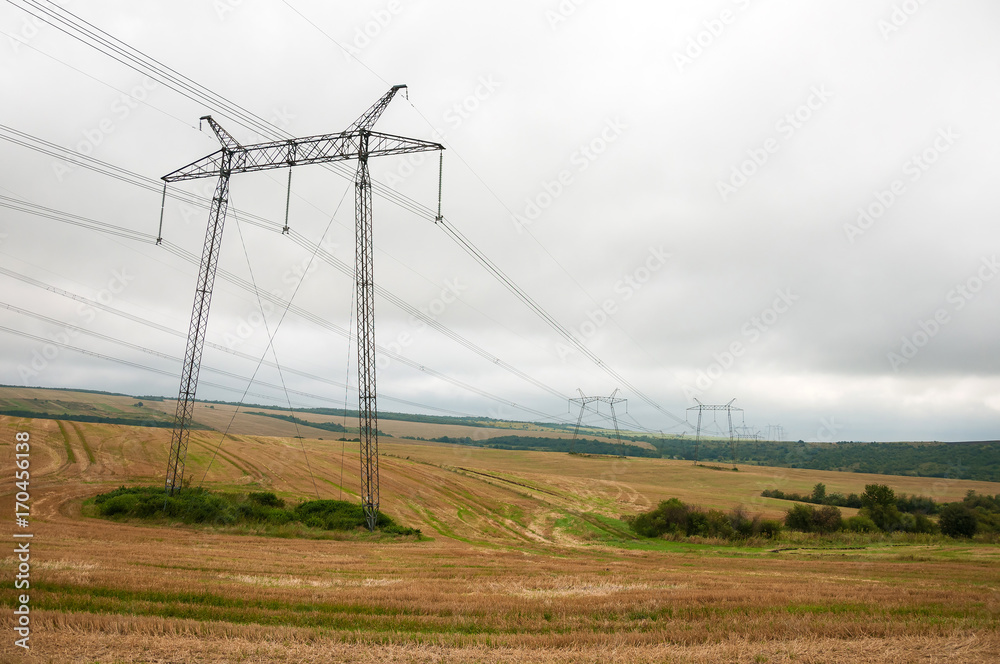 Power lines on the field in cloudy weather. Depressing scenery with power lines on the autumn field.