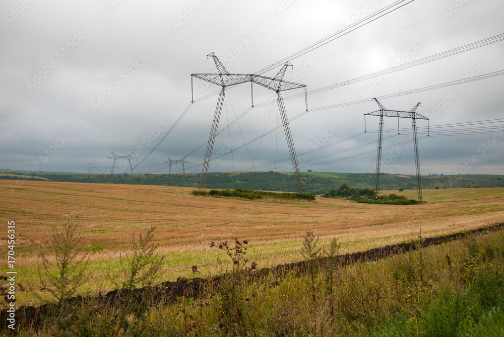 Power lines on the field in cloudy weather. Depressing scenery with power lines on the autumn field.