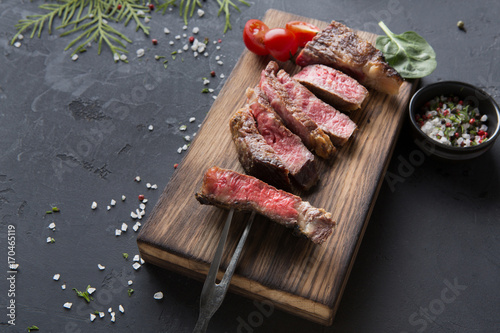 Rib eye steaks and spices on wood at black background