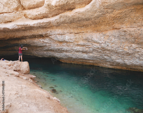 Female tourist taking photo of Oman's Bimmah sinkhole, one of the world most beautiful natural sinkhole in the Sultanate of Oman. Tourists can swim in the clear turquoise water