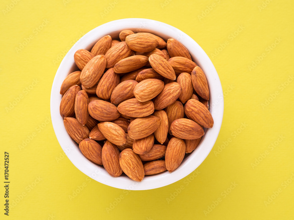 Top view of white cups, bowls with a handful of pecans, almonds on a bright yellow background color Top view of white cups, bowls with a handful of pecans, almonds on a bright yellow background color