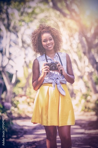Portrait of woman holding digital camera at park