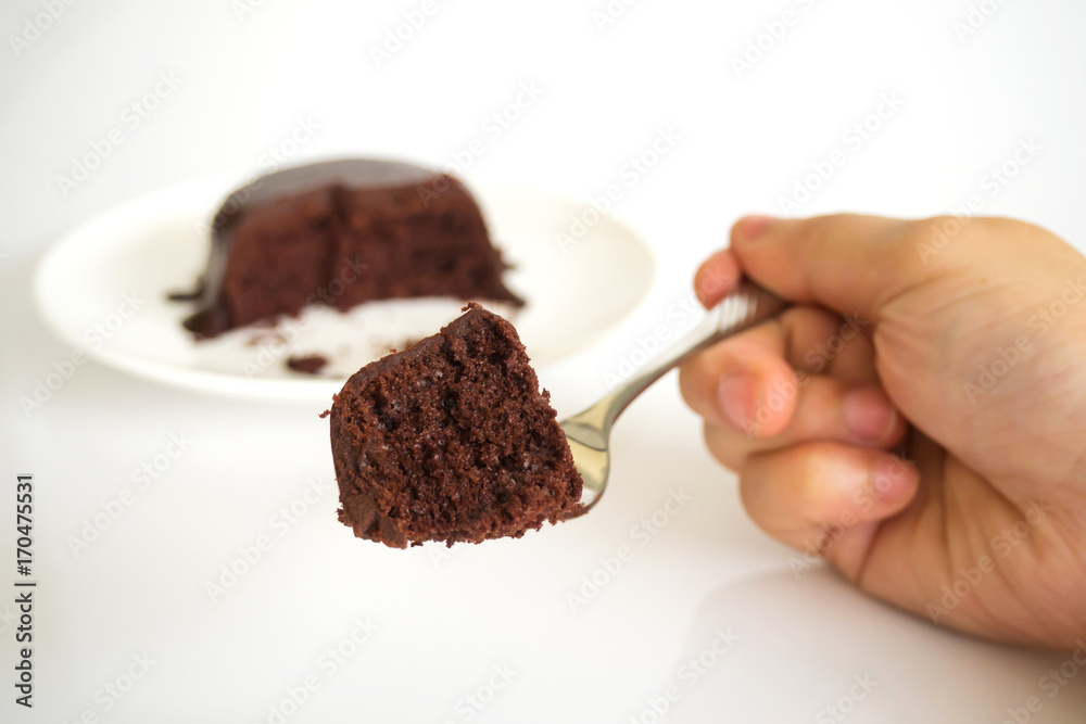 Woman hand holding fork served chocolate cake with chocolate fudge. Chocolate cake on white plate over white background are background. Favorite cake for chocolate lover. Woman hand holding fork served chocolate cake with chocolate fudge. Chocolate cake on white plate over white background are background. Favorite cake for chocolate lover.