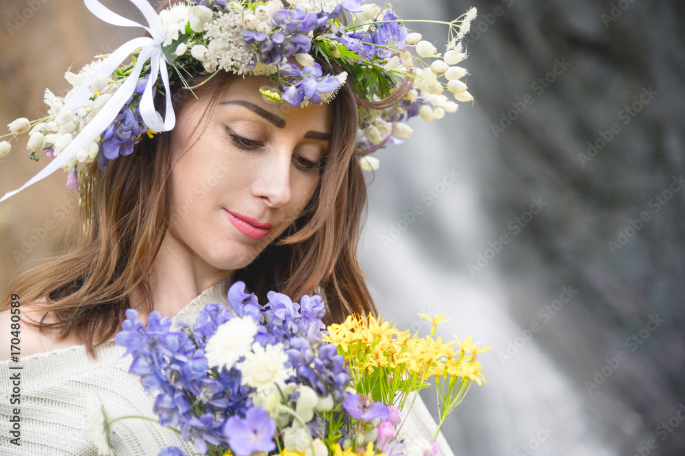 Portrait of a girl with a wreath on her head and a bouquet of flowers in her hands against a waterfall Portrait of a girl with a wreath on her head and a bouquet of flowers in her hands against a waterfall