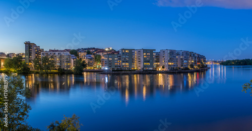 En vacker sommarnatt ser vi  belysningen i bostadshus på Lilla Essingens speglas i vattnet