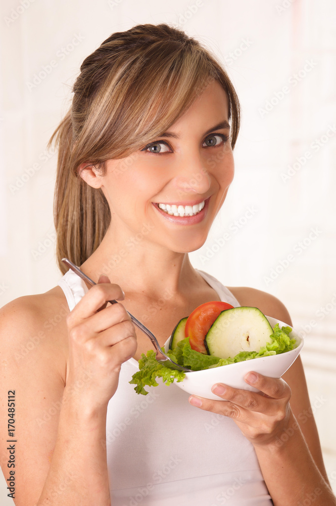 Beautiful young woman wearing a white t-shirt and holding in her hand a healthy salad and using a fork Beautiful young woman wearing a white t-shirt and holding in her hand a healthy salad and using a fork